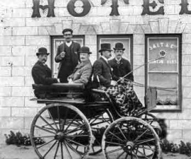 A small carriage with a group of smart gentlemen. Was the driver actually the individual standing at the back of the carriage?