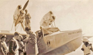 A reporter interviews passengers after a flight. Note the old wooden ladder used to access the cockpit and passenger accommodation. And the boy standing next to one engine while the propeller of the other is apparently still turning