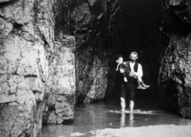 Children carried through the pool in front of the cave