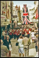 A band marches along the upper end of the street, flags flying probably for some Royal event