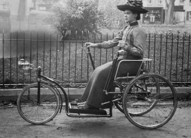 A lady rides an early tricycle along the Parade