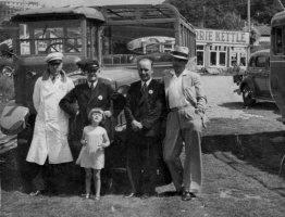 A group poses for a photograph in front of a bus. The Merrie Kettle can be seen in the background