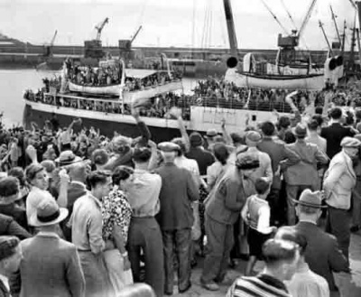 An evacuation boat leaving, watched by a large crowd
